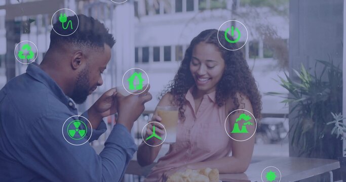 Chatting man and woman sipping orange juice at outdoor cafe terrace, with eco icons, potted plants