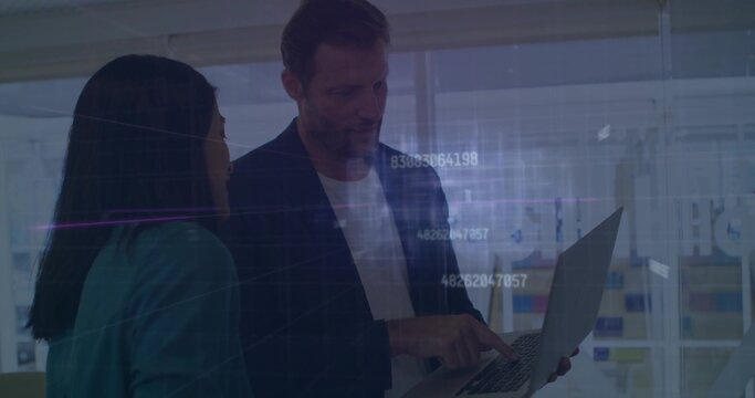 Pointing man and woman wearing suits collaborating on laptop in modern office, with data overlay