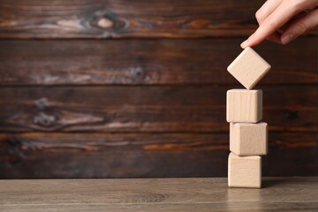 Woman moving cube at wooden table, closeup. Space for text