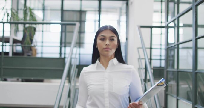 Walking worker holding documents through office stairway, metal railings glass panel potted plant