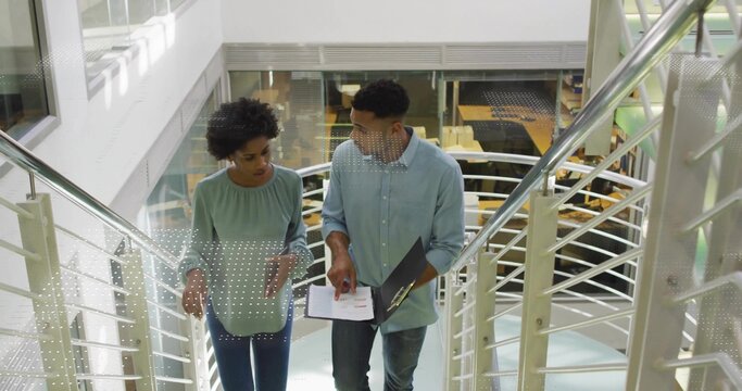 Coworkers ascending office atrium stairs reviewing clipboard charts with glass walls tables chairs - Powered by Adobe