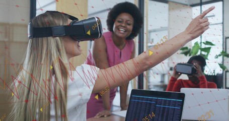 Woman wearing blouse and VR headset pointing forward in office, data overlay, laptops, copy space