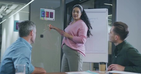 Pointing pregnant woman wearing pink top explaining phone mockups on whiteboard in conference room