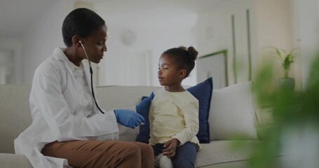 Fototapeta premium Doctor wearing lab coat and blue gloves using stethoscope on girl on sofa in living room