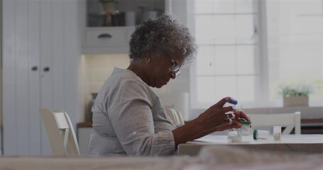 Senior woman with glasses sorting pills in kitchen, with pill bottles, container