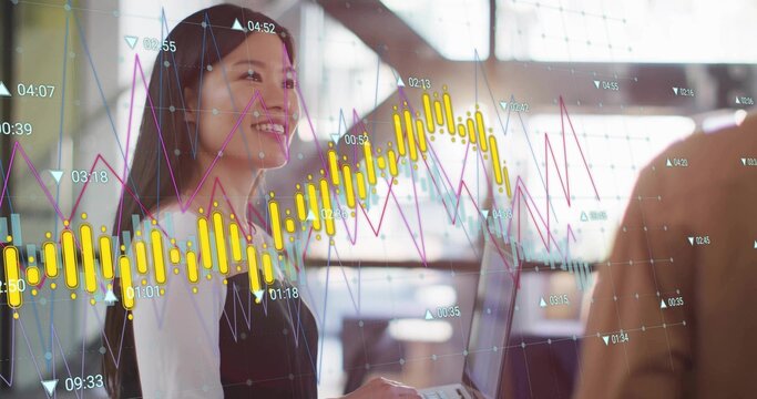 Holding laptop, Chinese businesswoman reviewing digital stock charts at modern office with coworker