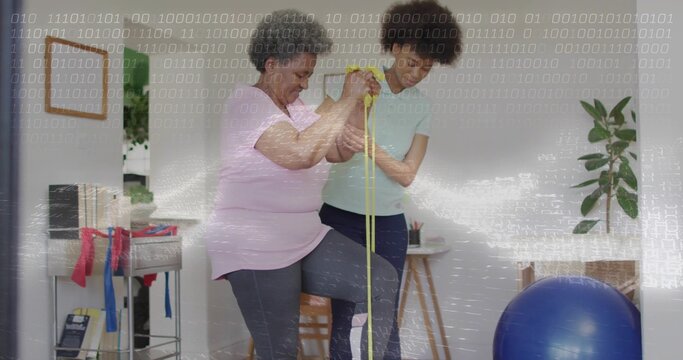Physiotherapist assisting senior balancing on one foot with yellow resistance band in rehab room