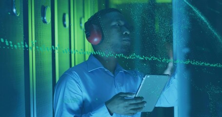 IT professional in blue shirt, red headphones scanning LED server racks using tablet in data center