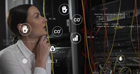 IT tech wearing blouse examining floating icons and cables beside racks in data center