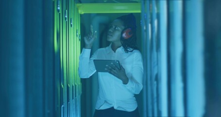 Inspecting female IT technician adjusting server module in data center aisle with tablet, earmuffs