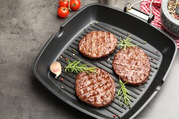 Pan with grilled patties, tomatoes and spices on grey table, closeup