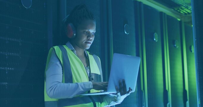 Technician checking racks in data center, with laptop earmuffs safety vest, copy space