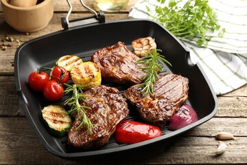 Pan with grilled beef steaks, rosemary and vegetables on wooden table, closeup