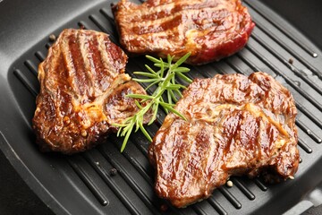 Grilled beef steaks, rosemary and peppercorns on black pan, above view