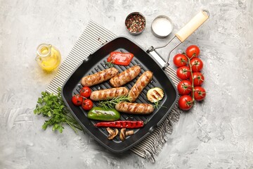 Pan with grilled sausages, vegetables, mushrooms and spices on gray textured table, flat lay