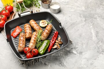 Pan with grilled sausages, vegetables, mushrooms and spices on gray textured table, closeup