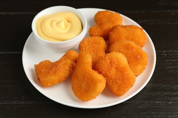 Tasty chicken nuggets with sauce on black wooden table, closeup