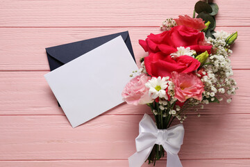 Blank card, envelope and flowers on pink wooden table, flat lay