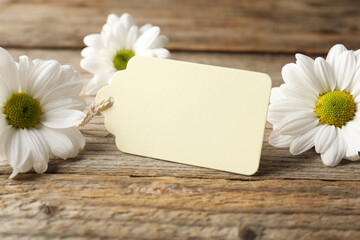 Blank tag and flowers on wooden table, closeup