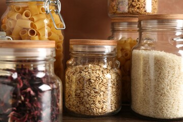 Glass jars with different products on wooden table, closeup