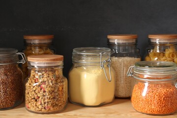 Glass jars with different products on wooden shelf, closeup