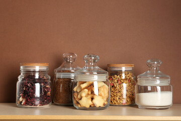 Glass jars with different products on wooden table against brown background