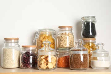 Glass jars with different products on wooden table near white wall