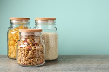 Glass jars with different products on grey table against light blue background. Space for text