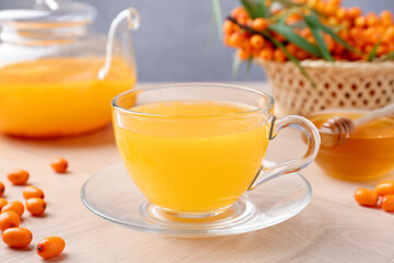 Sea buckthorn tea in glass cup, teapot, fresh berries and honey on wooden table, closeup