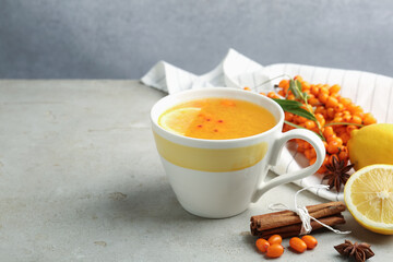 Sea buckthorn tea in cup, spices, lemon and fresh berries on light grey table, closeup. Space for text