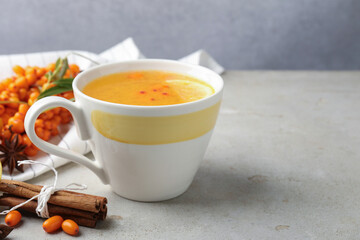 Sea buckthorn tea in cup, spices and fresh berries on light grey table, closeup. Space for text