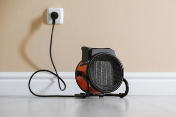 Electric fan heater on floor near beige wall indoors, closeup
