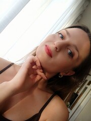 Close up portrait of a young attractive woman holding a smartphone and taking a selfie. Beautiful woman looking at camera and smiling. Pretty female with long hair, blonde takes selfie on mobile phone