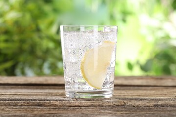 Refreshing water with lemon and ice on wooden table against blurred background