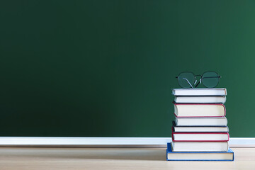 Happy Teacher's Day. Stack of books and glasses on wooden table near chalkboard, space for text