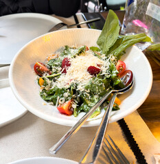 Fresh green salad with arugula, cherry tomatoes, raspberries, and grated cheese. Healthy and colorful meal served in a white bowl.