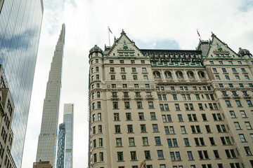 The historic Plaza Hotel with its ornate architecture stands beside modern glass skyscrapers in Midtown Manhattan. The contrast between old and new buildings highlights the diverse cityscape of New
