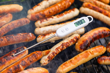 Raw sausages on barbecue with digital meat thermometer showing unsafe low temperature