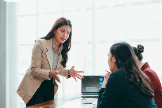Asian businesswomen arguing during a meeting, expressing frustration over financial charts displayed on a laptop at the corporate office