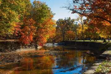 The Rocky River flows over a small spillway amid autumn foliage in Rocky River Reservation, part of the Greater Cleveland Ohio metro parks system.