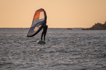 Wingfoiling in Brittany at sunset, a few rocks in the background