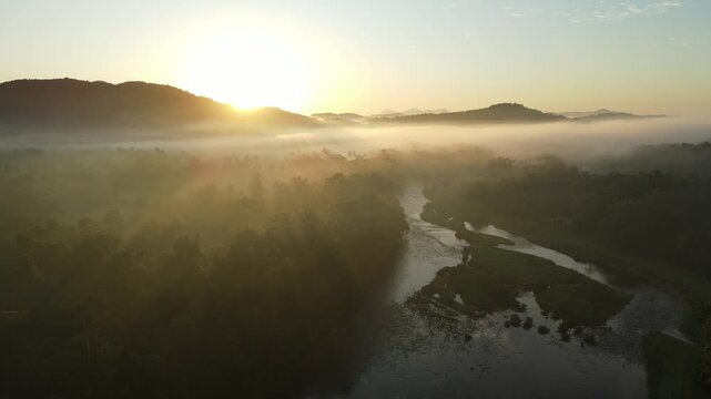 Vista a&eacute;rea com voo de drone ao nascer do sol rio nhundiaquara em Morretes no litoral do Paran&aacute; sobre a mata atl&acirc;ntica com vista para montanhas sob neblina com raios de sol