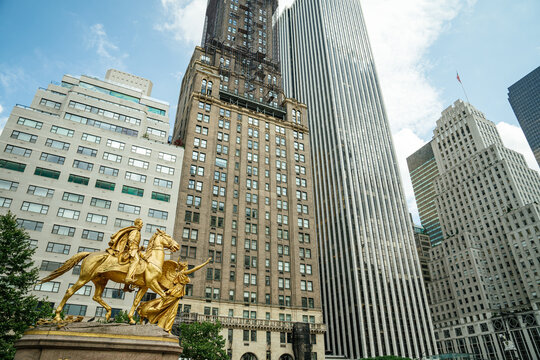 A striking view of the gilded William Tecumseh Sherman statue at Grand Army Plaza in New York City. Tall skyscrapers rise behind the monument under a bright summer sky, blending history and modern