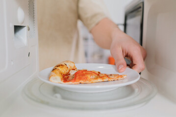Reheating a slice of leftover pizza on a white plate in a microwave oven.