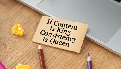 A sign that says If Content Is King Consistency Is Queen is on a desk with a pair of pencils and...