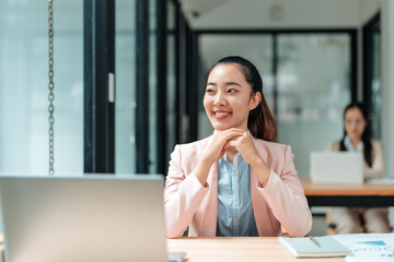 Portrait of a young Asian businesswoman smiling and thinking in a modern office, showing confidence...