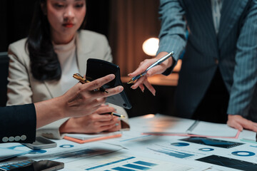 Business team working together on financial data, using calculator and pointing at charts during a late night meeting
