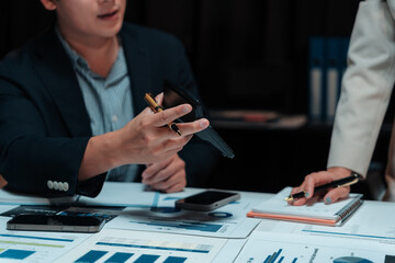 Business team working late at night, calculating and analyzing financial data on charts and graphs using calculator and smartphone