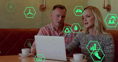 Man and woman opening laptop lid at cafe table activating green hexagon icons reviewing eco metrics - Powered by Adobe