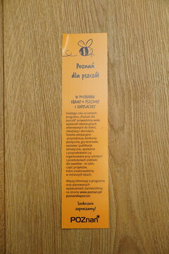 A yellow informational flyer titled 'Poznań dla pszcz&oacute;ł' encouraging bee-friendly activities on a wooden surface
